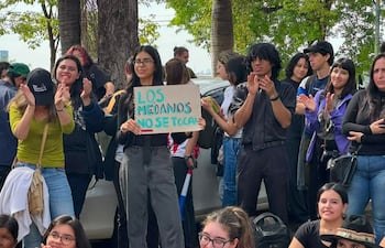 Mujer con gafas sostiene cartel 'LOS MEDANOS NO SE TOCAN', rodeada de personas aplaudiendo en un ambiente urbano.