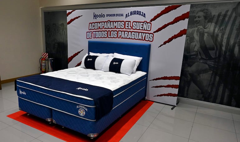 Mujer con vestimenta de selección paraguaya y hombre con chaqueta azul en evento formal de Koala y la APF, con logo de Albirroja visible.