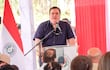 César Sosa con camisa oscura habla en un micrófono, rodeado de árboles y decoraciones en rojo y blanco.