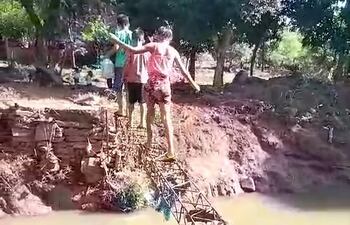 Los niños se arriesgan para cruzar la viga de metal que quedó tras el colapso del puente.
