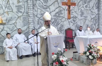 Monseñor Omar López, con mitra y capa blanca, habla frente a un micrófono, rodeado de clérigos y un altar decorado.
