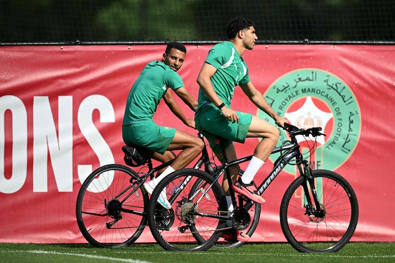 El mediocampista de Marruecos Azzedine Ounahi (I) y el defensor Achraf Hakimi (D) andan en bicicleta a su llegada a una sesión de entrenamiento durante el torneo de fútbol de la Copa del Mundo 2026 en The Pingry School en Basking Ridge, Nueva Jersey.