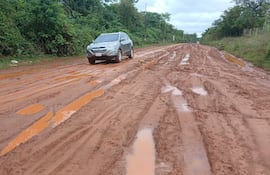 Un SUV gris avanza lentamente por un camino de tierra en mal estado, rodeado de densa vegetación y charcos de agua.