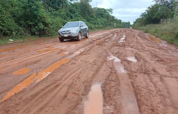 Un SUV gris avanza lentamente por un camino de tierra en mal estado, rodeado de densa vegetación y charcos de agua.