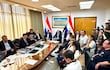 Yamil Esgaib , Raúl Latorre y Hugo Meza observan documentos mientras una mujer presenta en una oficina iluminada.