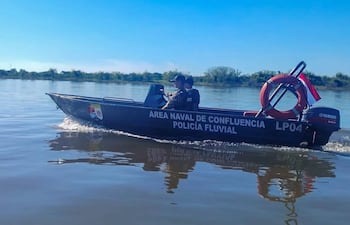 Agentes de la Policía Fluvial en lancha, uno al mando, vestidos con uniforme, rodeados de vegetación y cielo despejado.