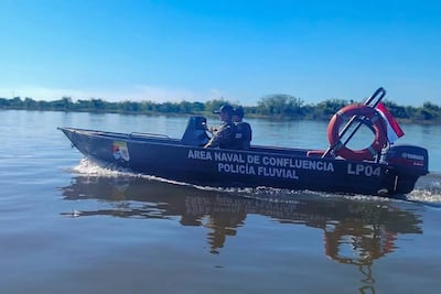 Agentes de la Policía Fluvial en lancha, uno al mando, vestidos con uniforme, rodeados de vegetación y cielo despejado.