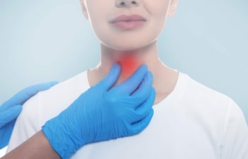 Mujer con camiseta blanca y expresión serena, mientras manos con guantes azules examinan su cuello en un fondo azul claro.