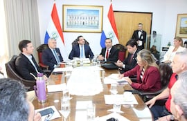 Félix Sosa y otros cinco hombres sentados alrededor de una mesa, con documentos y banderas de Paraguay al fondo, en un ambiente formal.