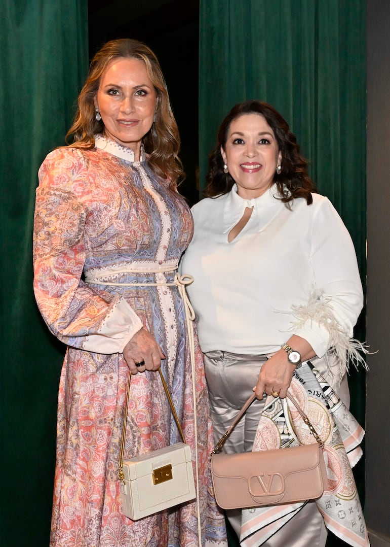 Soraya Bittar en vestido colorido junto a otra mujer en blusa blanca y pantalones plateados, ambas sonriendo en un ambiente festivo.