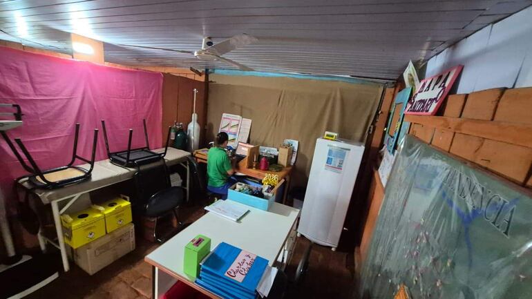 Persona de espaldas en camiseta verde, trabajando en escritorio con documentos, en ambiente de puesto de salud.