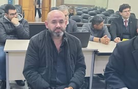 Gustavo Rodríguez con chaqueta negra y expresión seria, acompañado de hombres en suéter y otros con miradas preocupadas.