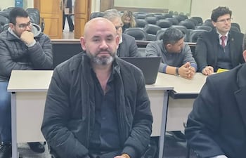 Gustavo Rodríguez con chaqueta negra y expresión seria, acompañado de hombres en suéter y otros con miradas preocupadas.