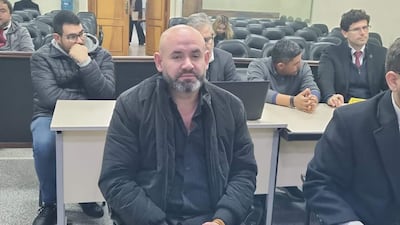 Gustavo Rodríguez con chaqueta negra y expresión seria, acompañado de hombres en suéter y otros con miradas preocupadas.