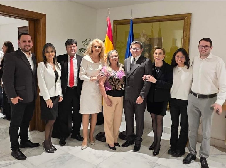 Mathías Villasanti y seis mujeres sonríen en fila, vistiendo atuendos formales, en un ambiente de celebración con banderas al fondo.