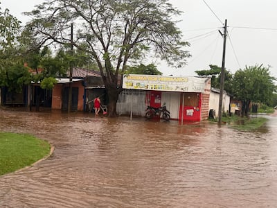 Persona caminando sobre agua en la calle, con un objeto en mano, mientras se observa un negocio con letrero.