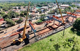 Estructura metálica en construcción sostenida por grúas amarillas, maquinaria pesada y un entorno urbano en desarrollo.