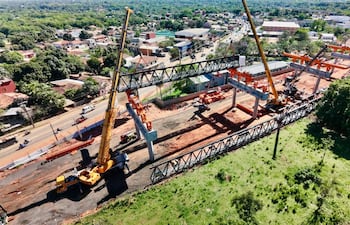 Estructura metálica en construcción sostenida por grúas amarillas, maquinaria pesada y un entorno urbano en desarrollo.