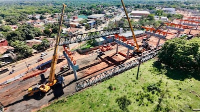 Estructura metálica en construcción sostenida por grúas amarillas, maquinaria pesada y un entorno urbano en desarrollo.