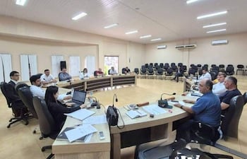 Hombres y mujeres vestidos formalmente en reunión, escuchando a un orador, con un ambiente de atención y seriedad.