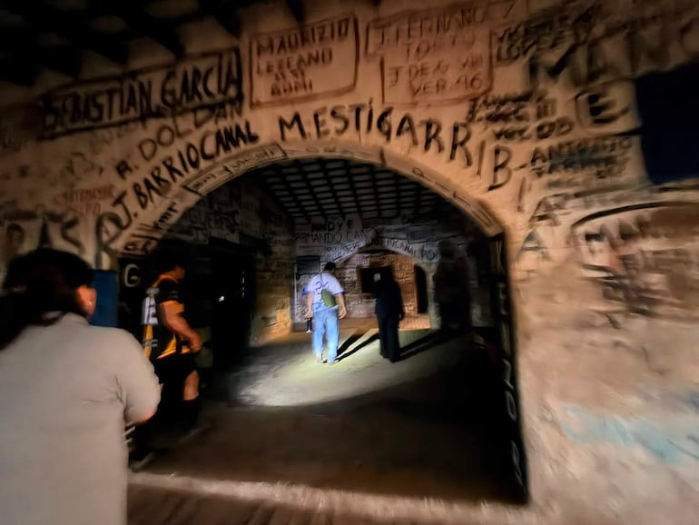 Tres personas en un espacio interior decorado con graffitis; una mujer y dos hombres en diferentes posturas y vestimentas diversas.