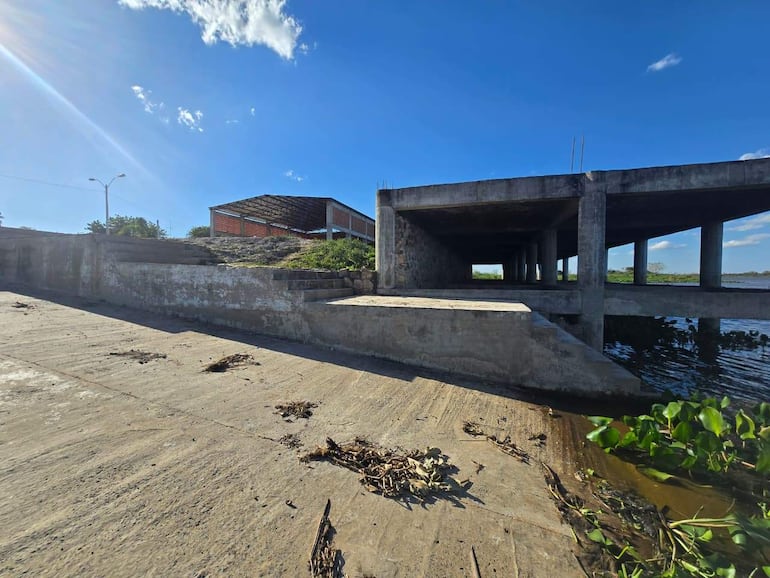 Estructura de hormigón y ladrillo inacabada junto a un muelle, en un entorno deshabitado.