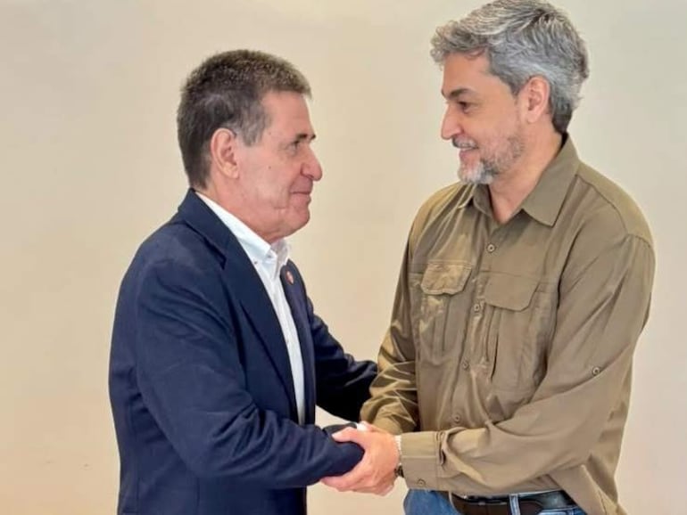 Cartes, con saco oscuro y camisa blanca, y Abdo Benítez, en camisa clara y jeans, se saludan sonriendo en un ambiente interior.