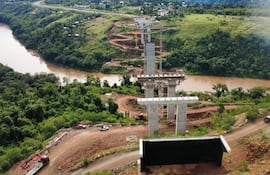 Vista aérea de la obra en construcción del puente sobre el río Monday, rodeado de vegetación y maquinaria de construcción.