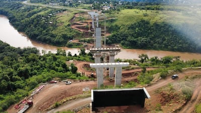 Vista aérea de la obra en construcción del puente sobre el río Monday, rodeado de vegetación y maquinaria de construcción.