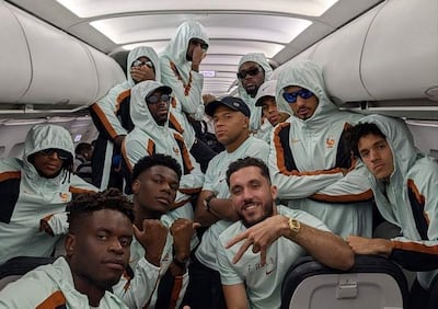 Jugadores del equipo francés de fútbol en avión, todos con chaquetas celestes, algunas personas usando gafas de sol y gorras, mostrando sonrisas.