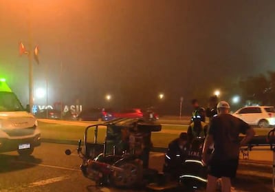 Vehículo de emergencia con luces verdes en una escena de neblina, mientras varias personas en uniforme asisten a un hombre herido.