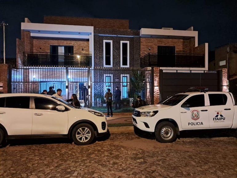 Personas reunidas frente a vivienda, un hombre en el centro parece ser Roberto Cubilla Sanabria. Vehículo policial de Itaipú a la derecha.