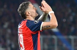 Jugador de Cerro Porteño, vistiendo camiseta roja y azul con el número 19, celebra con gesto de agradecimiento en estadio lleno de aficionados.