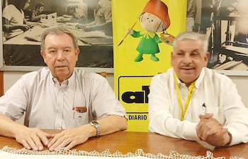 Isaías Fretes con camisa clara y Oscar Sánchez con camisa blanca, ambos conversando en un entorno de oficina, Fretes sério y Sánchez sonriendo.