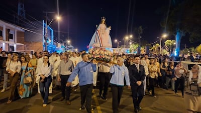 Grupo de personas lleva un altar con la Virgen del Rosario, iluminando la festividad con flores y banderas en una calle de Coronel Oviedo.