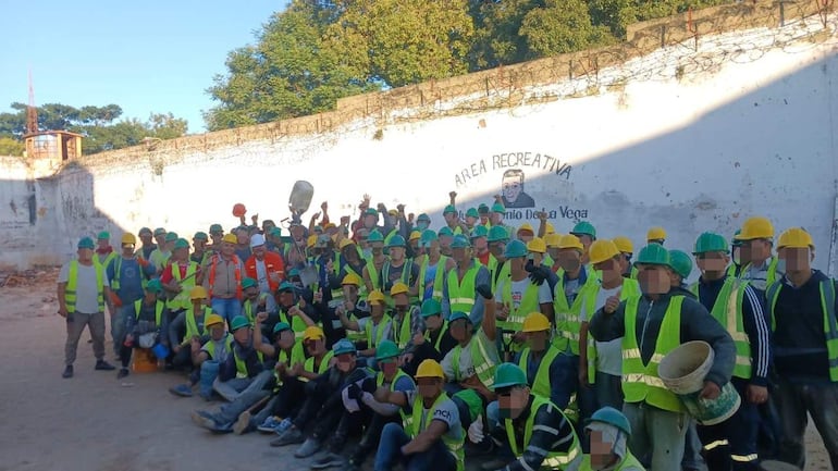 Grupo de trabajadores con chalecos reflectantes y cascos, levantando los brazos en señal de celebración en un espacio de construcción.