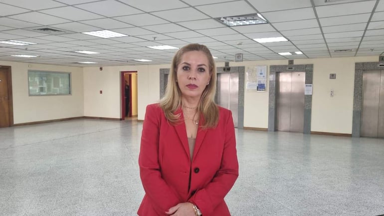 Ruth Benítez, mujer de traje rojo y cabello rubio, posando en un pasillo con puertas al fondo.