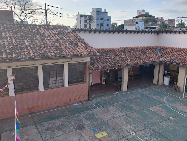 Patio de escuela con edificio rosa y banderines de colores en un ambiente desierto tras tormenta.