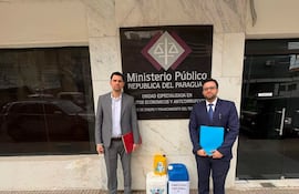 Pablo Callizo con traje gris y carpeta roja, junto a otro hombre en traje oscuro y carpeta azul, frente al Ministerio Público.