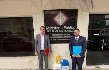 Pablo Callizo con traje gris y carpeta roja, junto a otro hombre en traje oscuro y carpeta azul, frente al Ministerio Público.