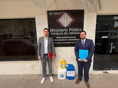Pablo Callizo con traje gris y carpeta roja, junto a otro hombre en traje oscuro y carpeta azul, frente al Ministerio Público.