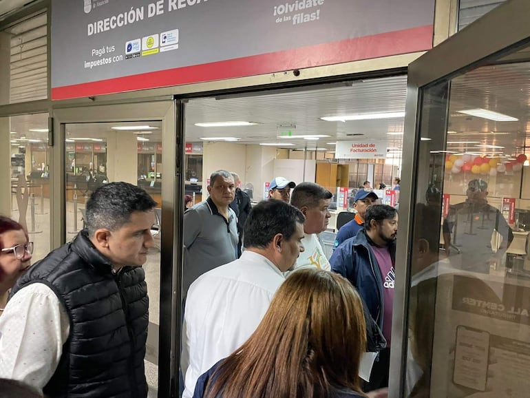 Roberto Cubilla Sanabria en camiseta blanca y chaqueta oscura conversa con otro hombre en un ambiente de oficina pública.