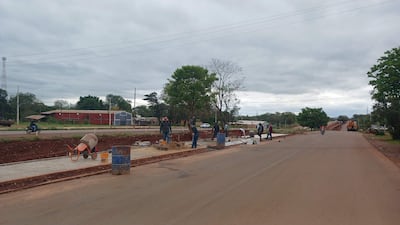 Trabajadores con cascos realizan tareas de pavimentación en la Ruta PY02, rodeados de herramientas y un camión en un día nublado.