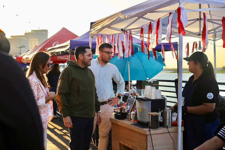 Luis Bello con chaqueta verde sonríe en evento costero, rodeado de personas y carpas, con buen ambiente.