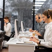 Cinco trabajadores en oficina de contacto, dos hombres y tres mujeres, utilizan auriculares y trabajan en computadoras.