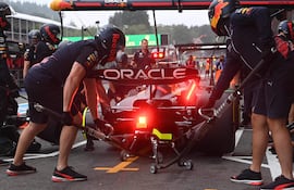 Mecánicos en uniforme oscuro trabajan en auto de Red Bull Racing, con un mecánico usando pistola neumática para cambiar llantas.