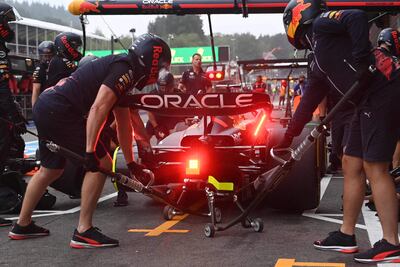 Mecánicos en uniforme oscuro trabajan en auto de Red Bull Racing, con un mecánico usando pistola neumática para cambiar llantas.