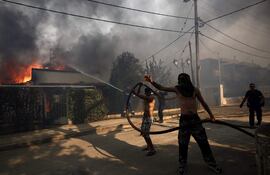 Bomberos y voluntarios trabajan en las tareas de extinción del fuego en la localidad de Kryoneri que ha obligado a evacuar a la población, este sábado.