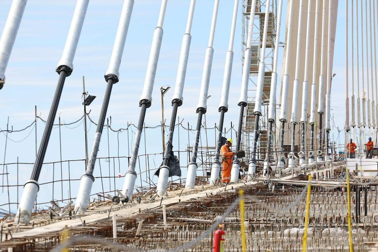Grupo de trabajadores de construcción con ropa de seguridad, uno sostiene una herramienta mientras supervisan el avance del puente Bioceánico.