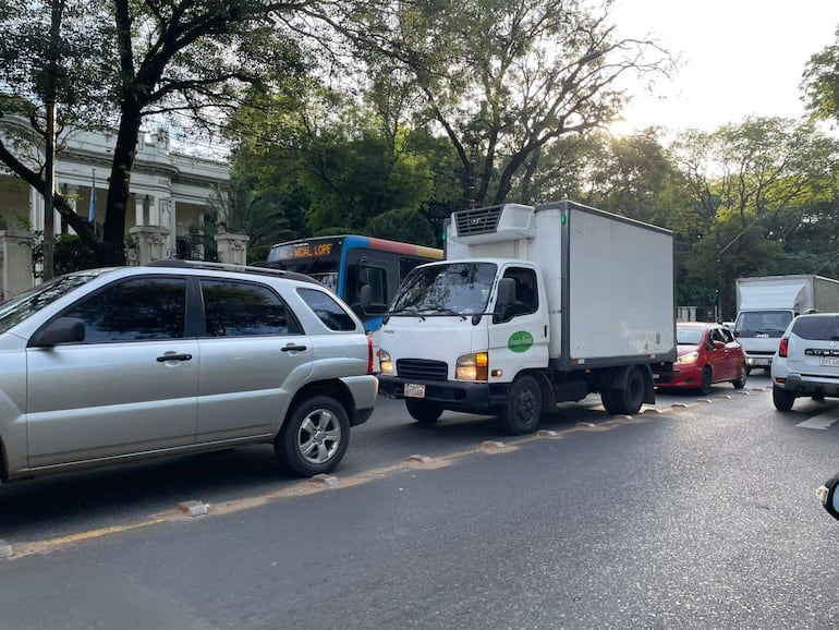 Escena de congestión vehicular en Mariscal López, con varios vehículos, incluyendo un camión de reparto y un elegante edificio de fondo.